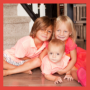 Toddler boy with longer hair in shorts and polo. Toddler girl in a pink tye die dress with blonde hair. Baby boy in a pink polo. All hugging and posed in front of the stairs. 